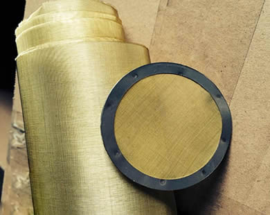 A roll of brass wire mesh and a round brass filter disc with rubber wrapping edge are placed together.